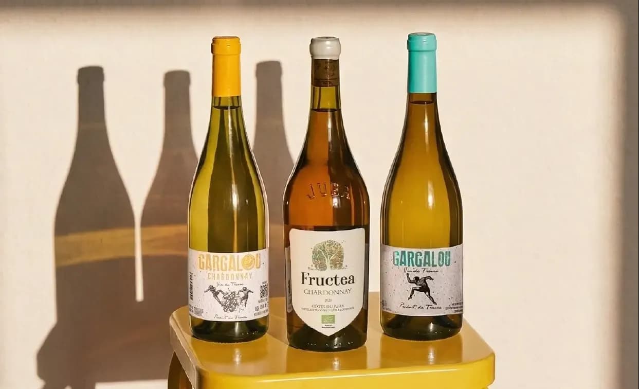 Three distinct bottles of white wine on a yellow surface with wall shadows.