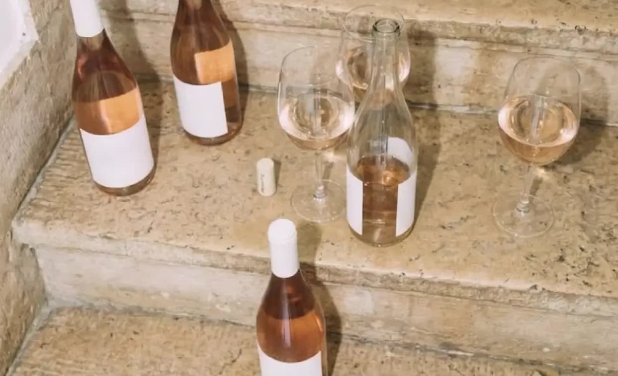 Several rosé wine bottles and glasses are placed on marble steps outdoors.