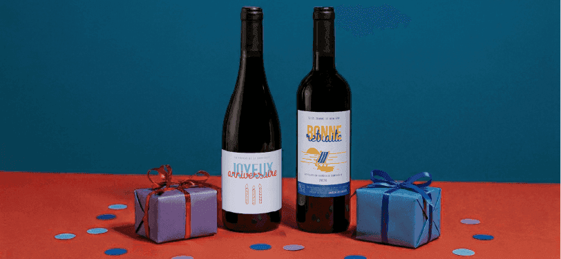 Two wine bottles and two gift-wrapped boxes with confetti on a red and blue background.