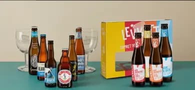 An assortment of craft beer bottles, two empty chalice glasses, and a yellow gift box.