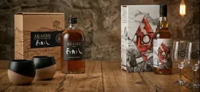Akashi Sake whisky bottles, decorative boxes, and two types of drinking glasses on wood.