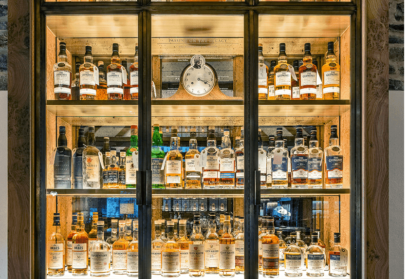 An illuminated glass cabinet filled with numerous bottles of various whiskies and spirits.