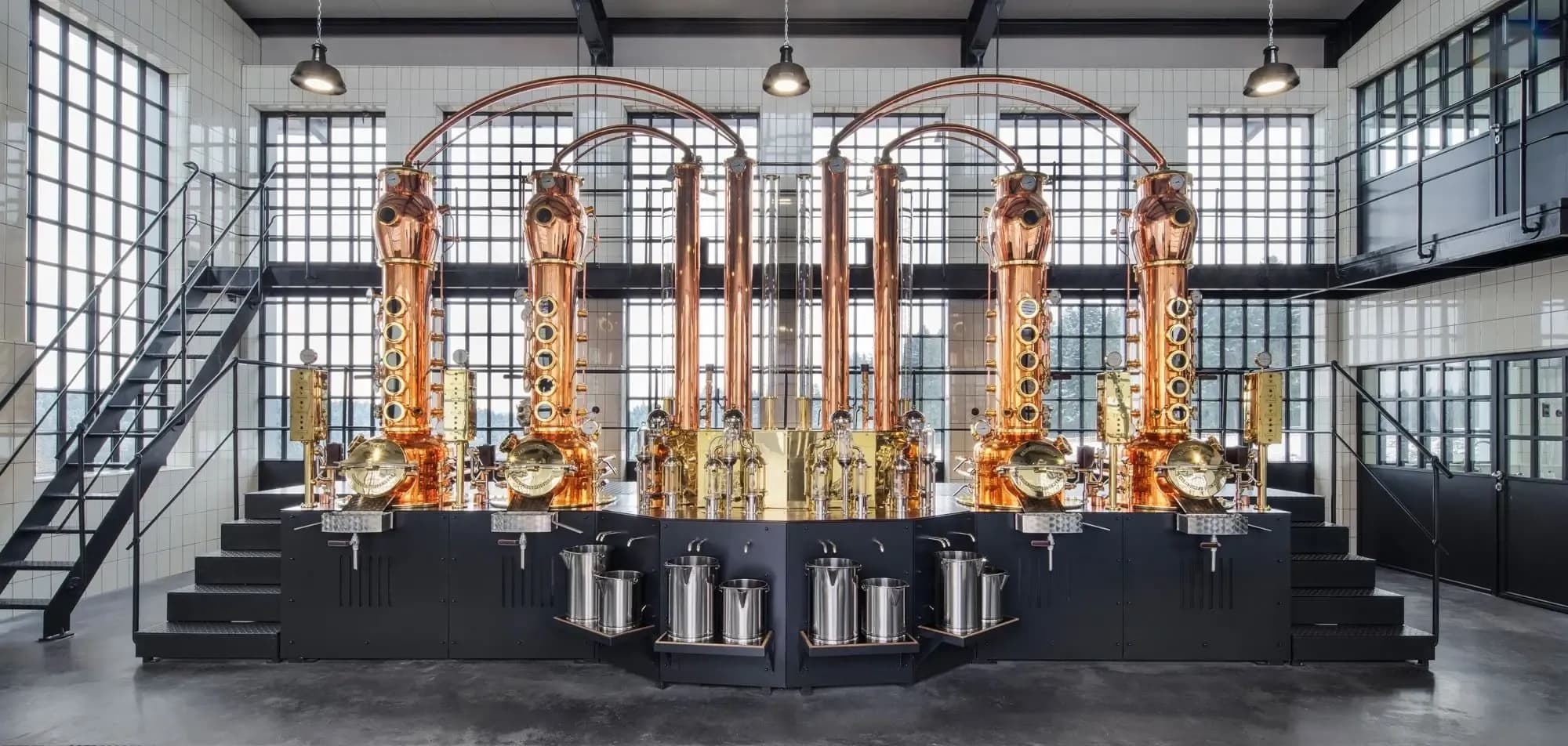 Copper stills gleam in a spacious, modern distillery with large industrial windows.