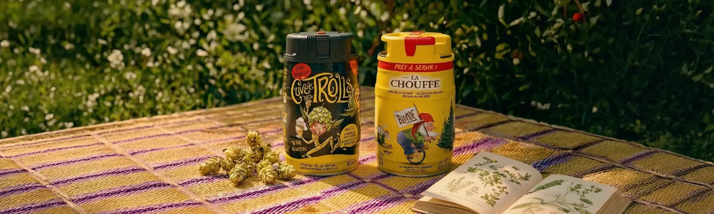 Two spice shakers, one black and one yellow, sit on a striped picnic blanket outdoors.