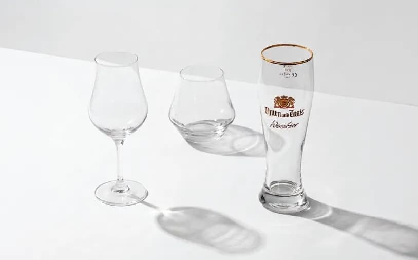 Three clear glass drinkware items, including a stemmed glass, a stemless glass, and a branded beer glass.