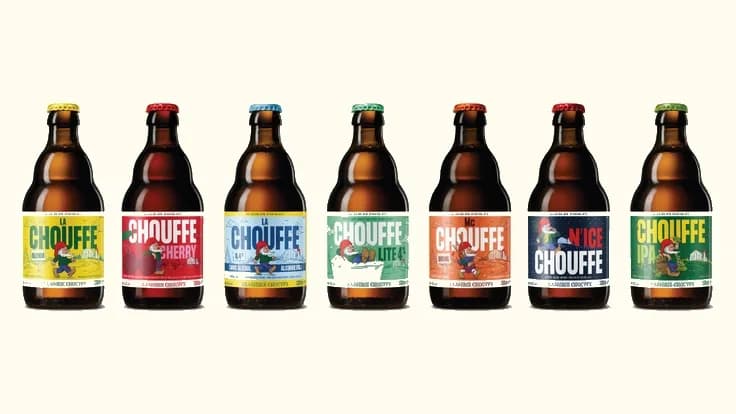 Seven Chouffe beer bottles with colorful labels featuring gnomes, displayed in a row.