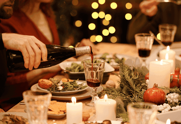 Person pouring red wine into a glass at a festive dinner table with lit candles.