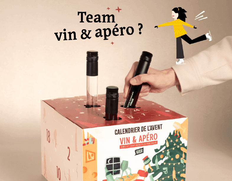 Hand placing a mini wine bottle into a 'Vin & Apéro' advent calendar with Christmas decorations.