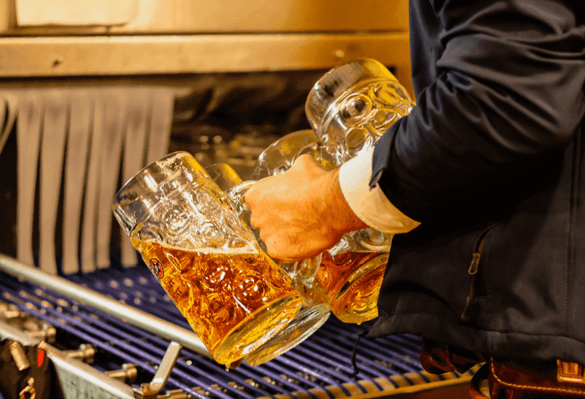 Person in traditional attire carrying multiple full beer steins, ready for serving.