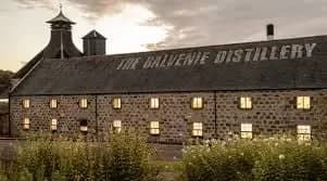 Stone building with THE BALVENIE DISTILLERY text and pagoda roof under a cloudy sky.