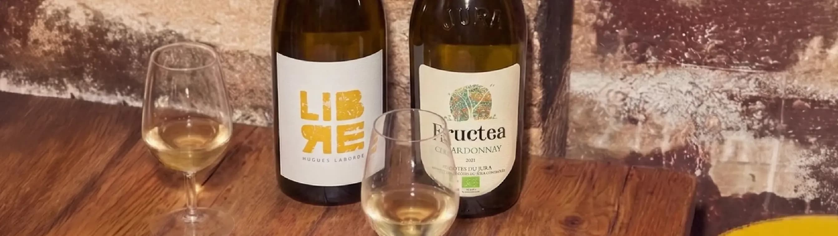 Two white wine bottles, one labeled "LIBRE", and two glasses on a wooden table.