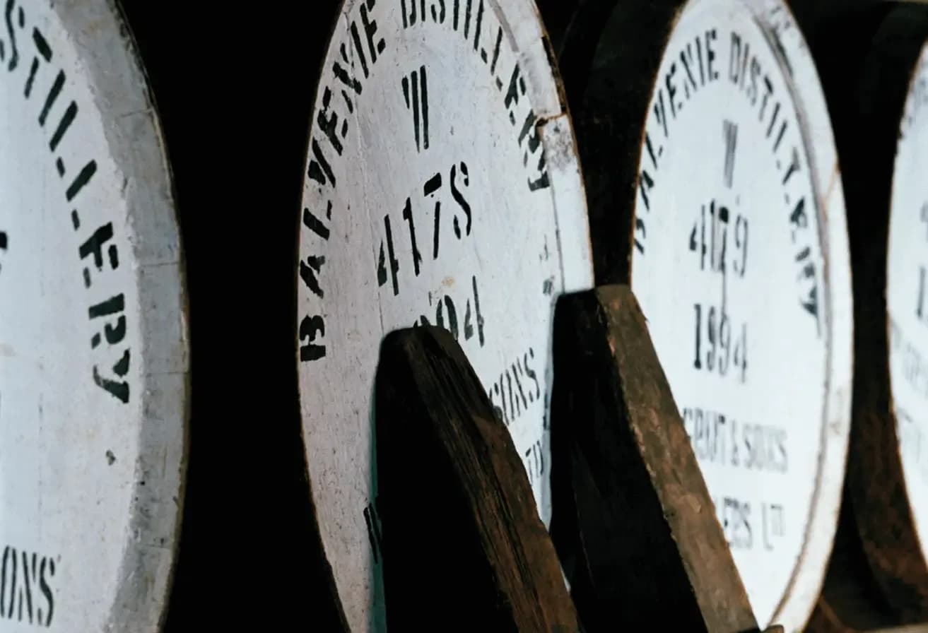 White-painted wooden Balvenie Distillery barrels marked 417S and 1994 in a dark cellar.